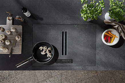 Moderne Induktionskochplatte mit elegantem Design, die eine Pfanne mit Pilzen zeigt, umgeben von minimalistischem Küchengeschirr und frischen Kräutern.